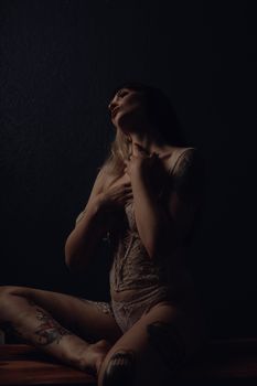 A woman in lingerie poses gracefully in a dimly lit room, conveying elegance and sensuality.