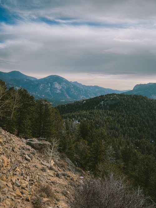 Free Breathtaking view of the Rocky Mountain range, with lush green forests and rocky terrain under a cloudy sky. Stock Photo