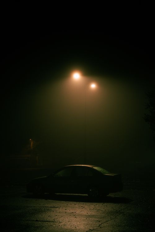 Free A silhouette of a car parked under a glowing streetlamp at night. Stock Photo
