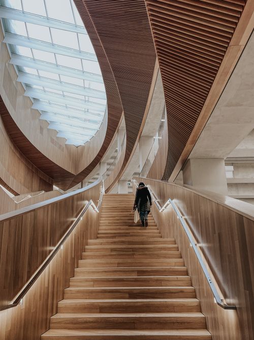 Free Woman walking up stairs inside Calgary's Central Library, showcasing modern architecture. Stock Photo