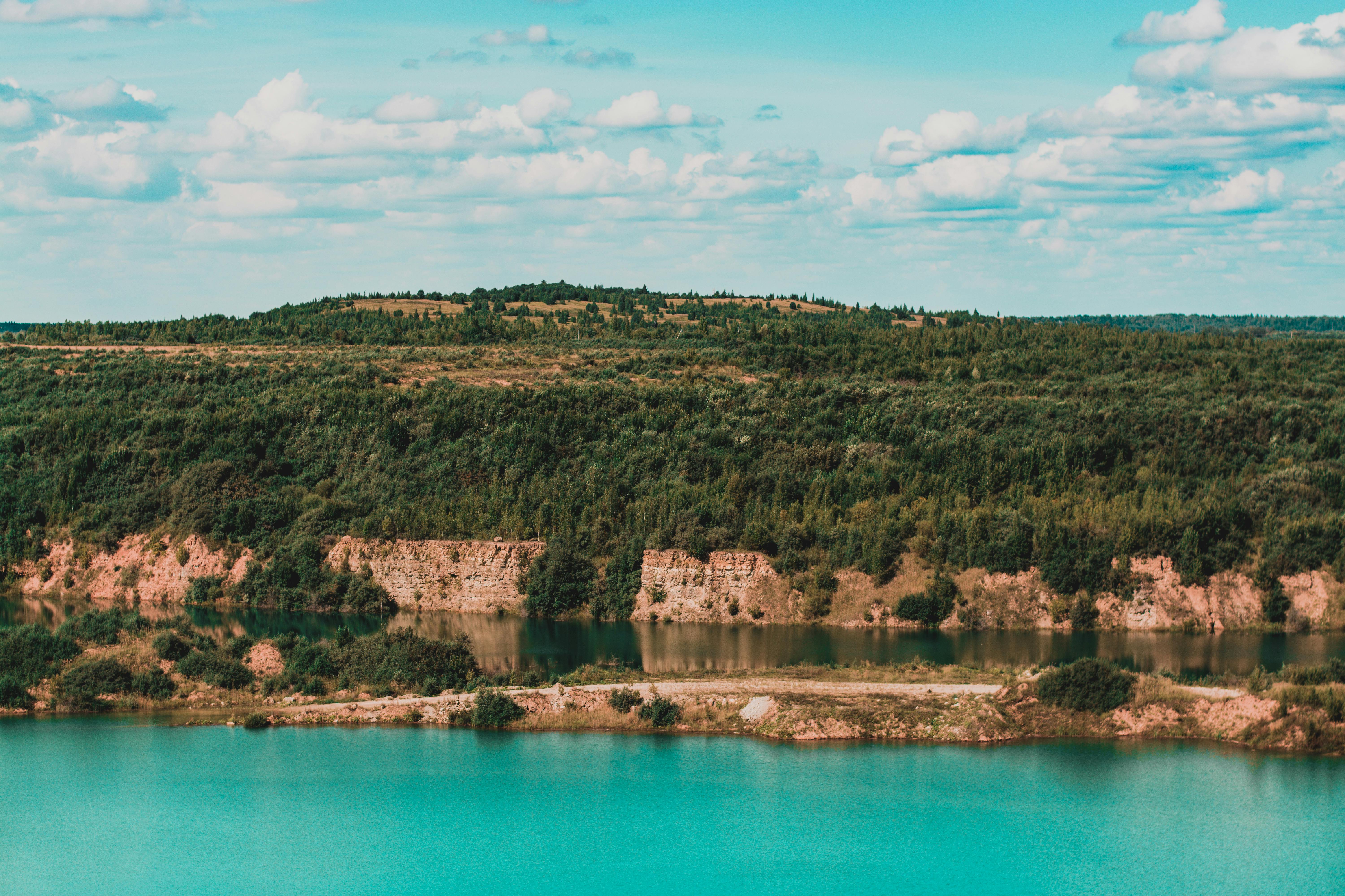 明亮的天空下，茂密的森林与宁静的蓝色湖泊构成了一幅迷人的景观