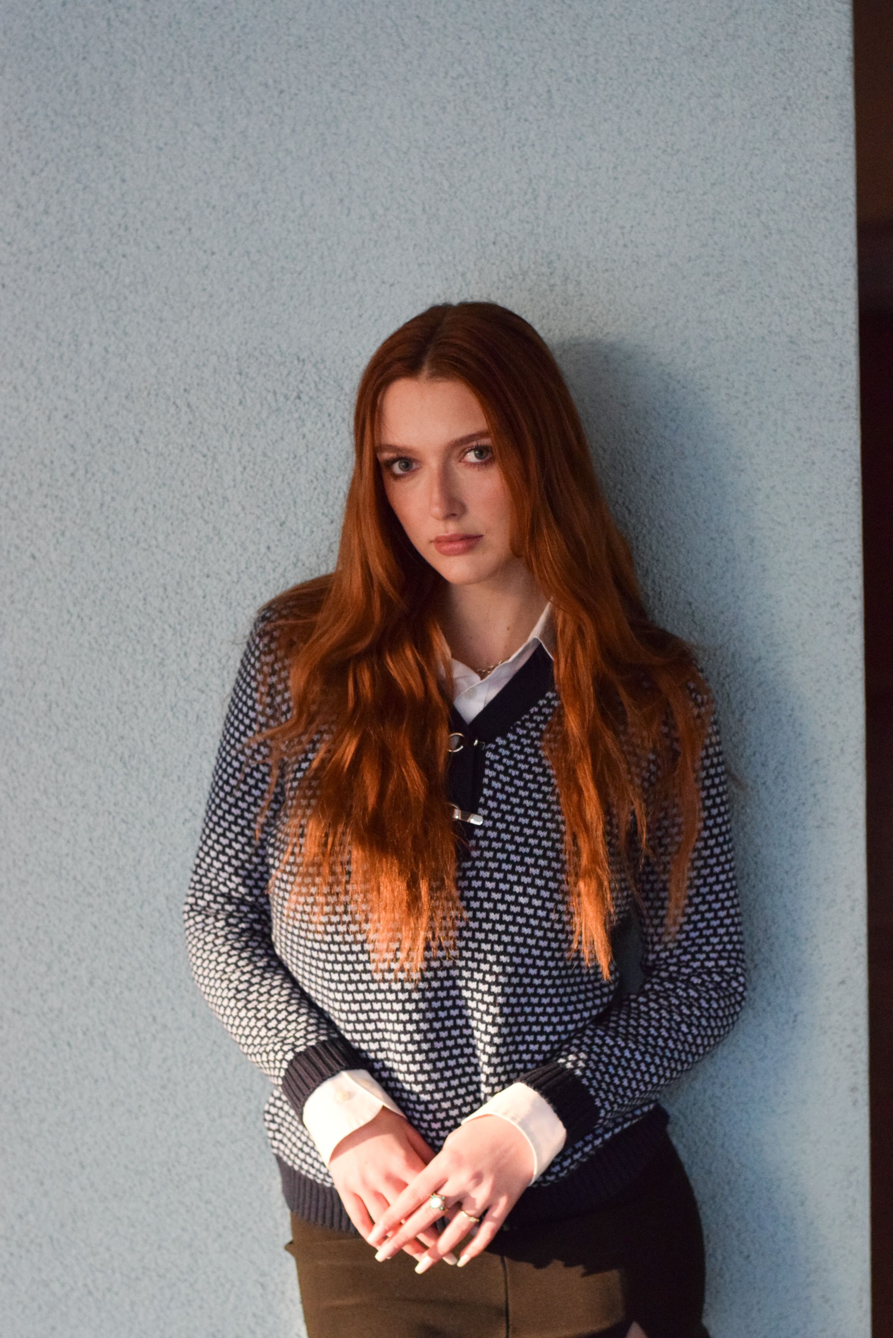Fashionable woman with auburn hair and stylish sweater posing indoors.