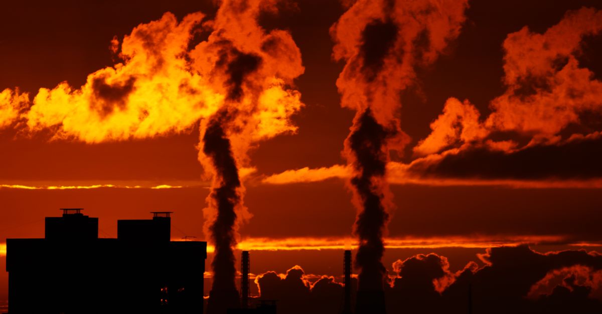 Dramatic industrial skyline silhouette with smoke against a vibrant orange sunset in Saint Petersburg, Russia.