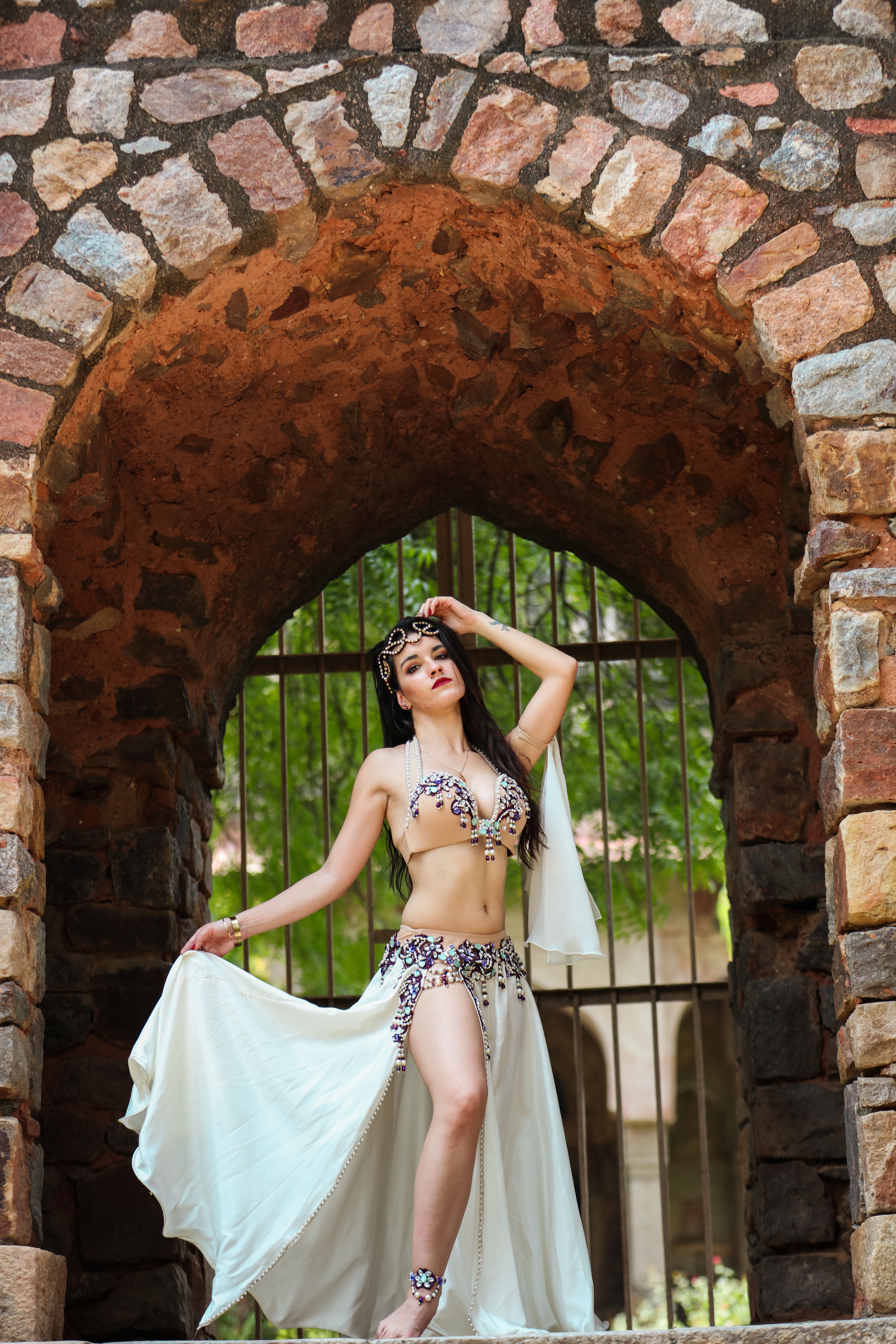 A woman in a dance costume poses gracefully under a stone archway.