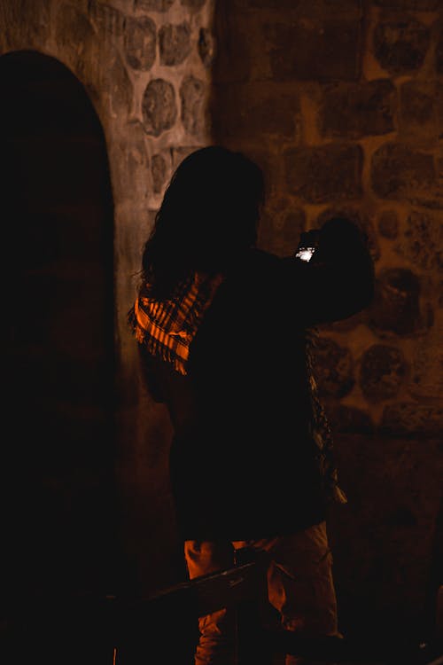Back View of Woman Standing by Stone Wall at Night