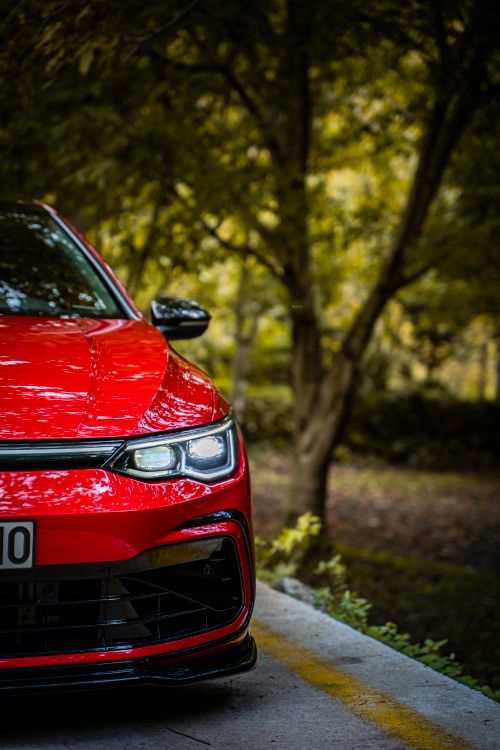 Free A vibrant red car parked on a forest road during daytime. Stock Photo