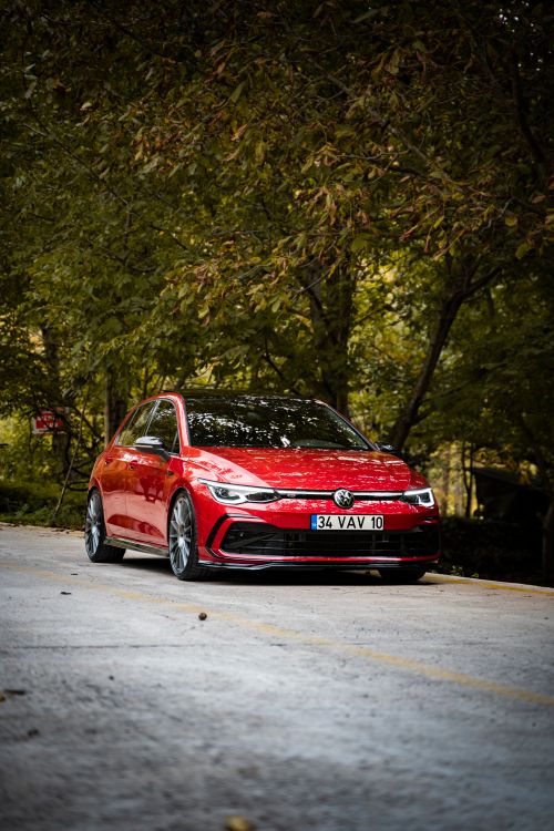 Free A vibrant red Volkswagen Golf GTI parked on a serene road lined with fall foliage, showcasing its sporty design. Stock Photo