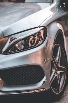 Detailed view of a sleek silver car's headlight and wheel, emphasizing modern automotive design.