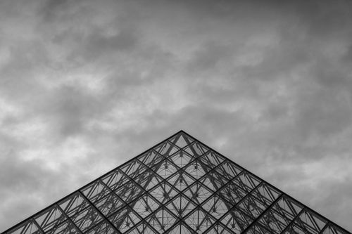 Free Dramatic black and white shot of the Louvre Pyramid in Paris with cloudy skies. Stock Photo