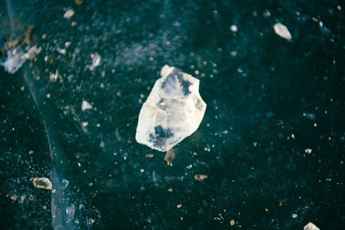 Free Macro image of a transparent crystal shard on a textured dark green surface, showcasing natural beauty. Stock Photo