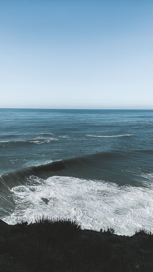Free Calm ocean waves crashing gently under a clear blue sky. Perfect for nature lovers. Stock Photo