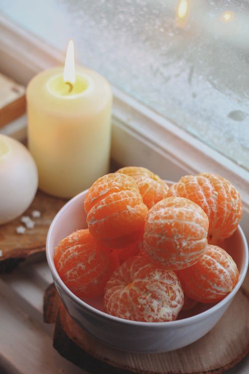 Free Warm and cozy scene of peeled tangerines in a bowl beside a burning candle on a windowsill. Stock Photo