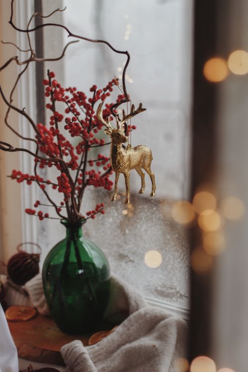 Free A warm festive scene with a golden deer ornament, red berries, and a vase on a windowsill. Stock Photo