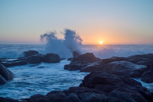 在开普敦风景优美的海岸线上，海浪拍打着岩石海岸，映衬着鲜艳的日落