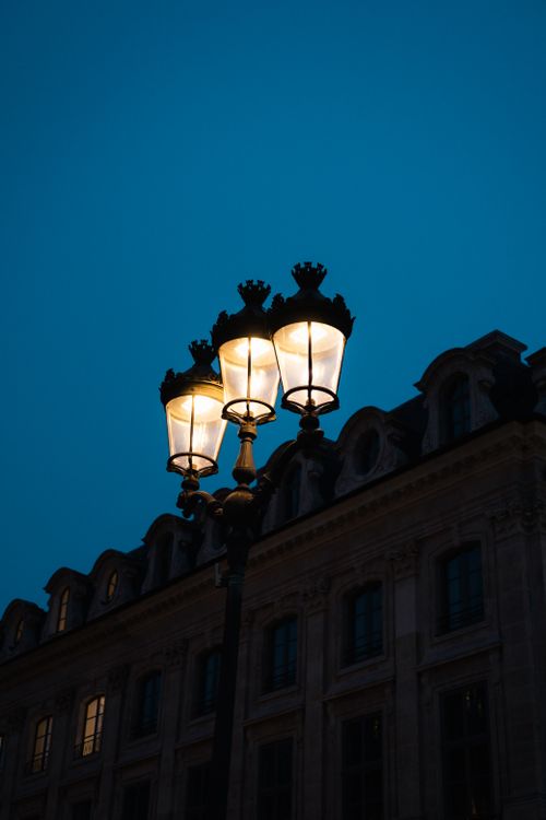 Free Illuminated vintage lamp posts with an elegant facade backdrop during twilight. Stock Photo
