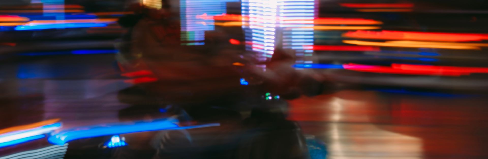 Blurred motion capture of a neon-lit amusement park scene, full of vibrant colors and lights.