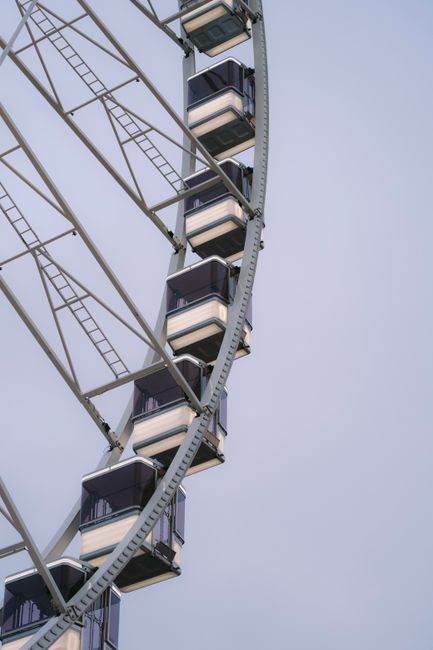 A detailed view of a modern ferris wheel with enclosed glass cabins against a clear sky.