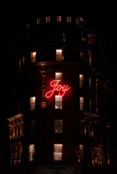 Nighttime view of a London building illuminated with a glowing 'Joy' sign, highlighting urban architecture.