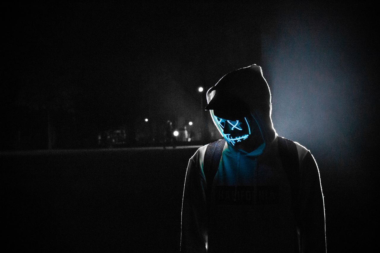 a mysterious figure wearing a led mask and hoodie stands illuminated i