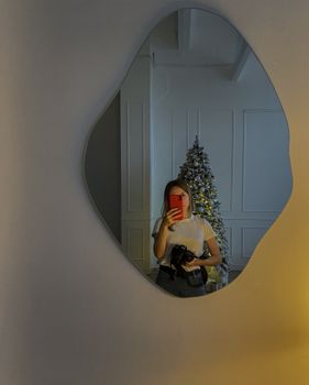 Woman taking mirror selfie with Christmas tree in background.