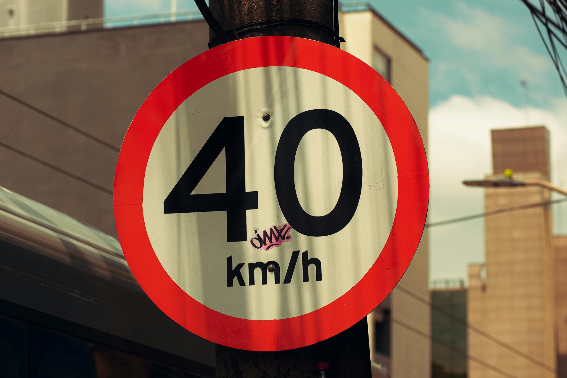 Close-up of a 40 km/h urban speed limit sign with graffiti in a city setting.