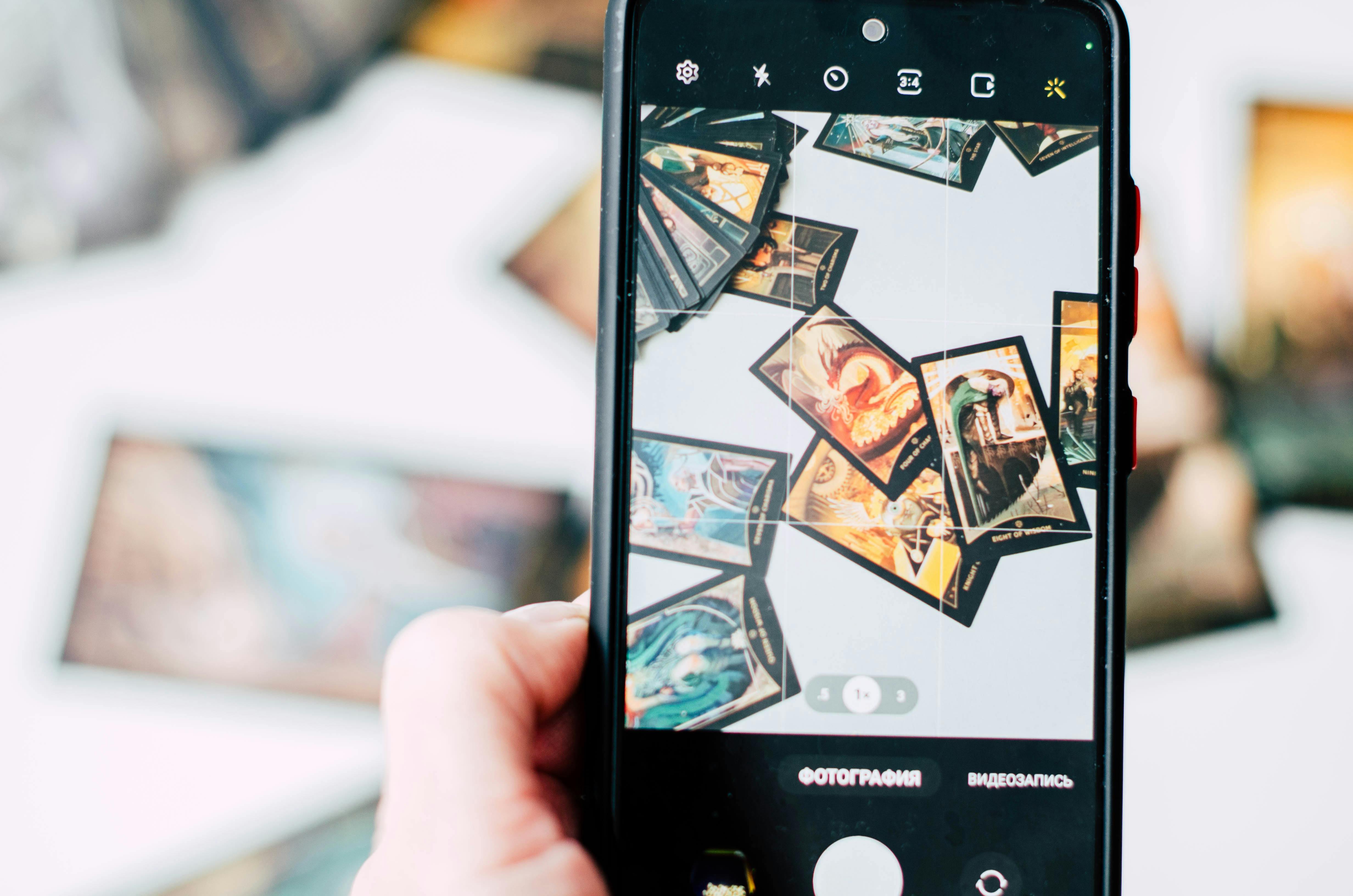 Free Hand holding smartphone capturing colorful tarot cards in focus. Stock Photo