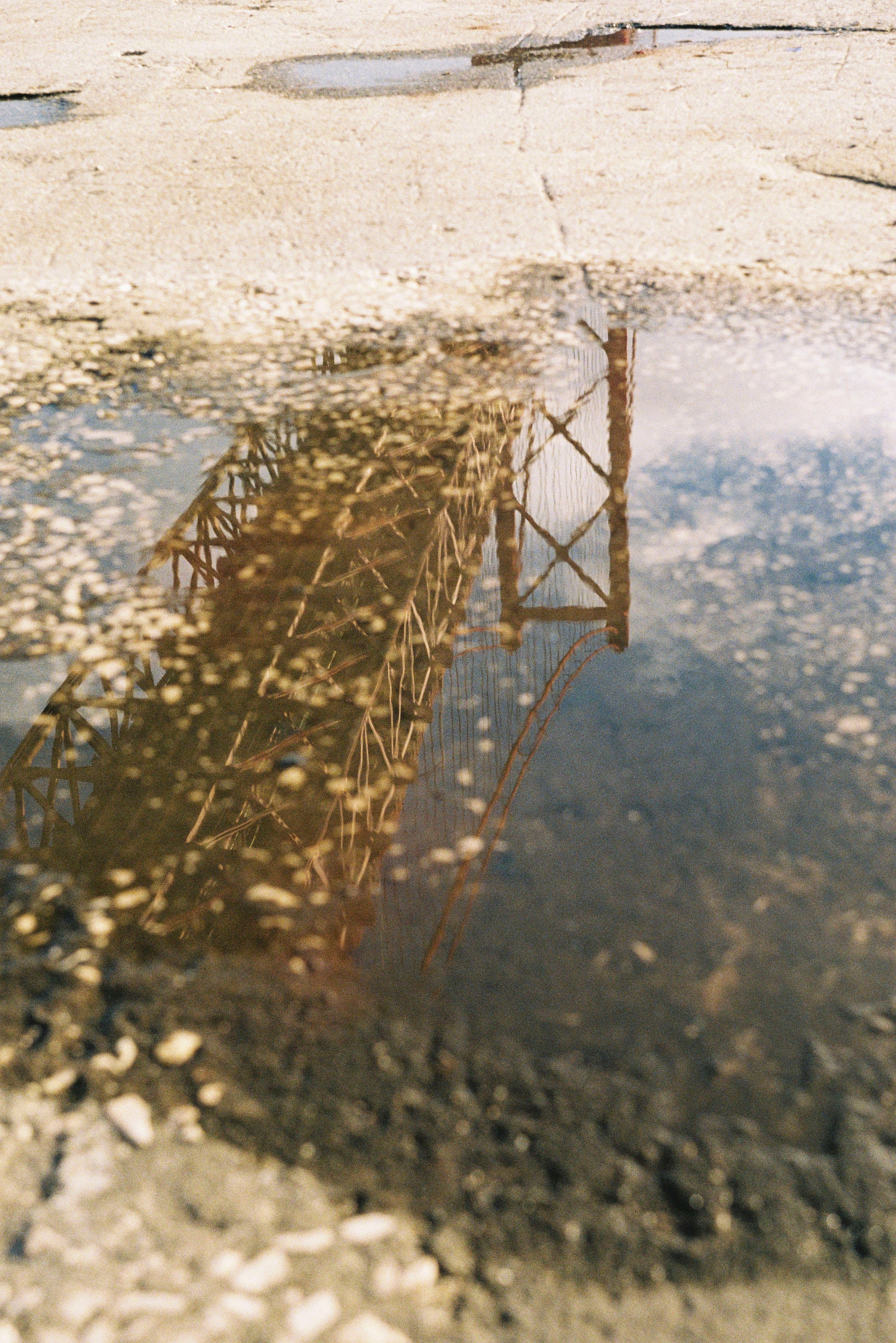 Reflection of a Lisbon bridge in a puddle on a sunny day, capturing urban essence.