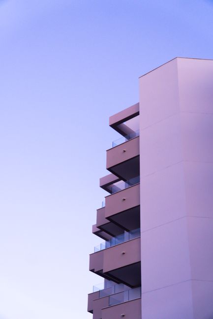 Contemporary building featuring glass balconies under a bright blue sky, showcasing modern architecture.