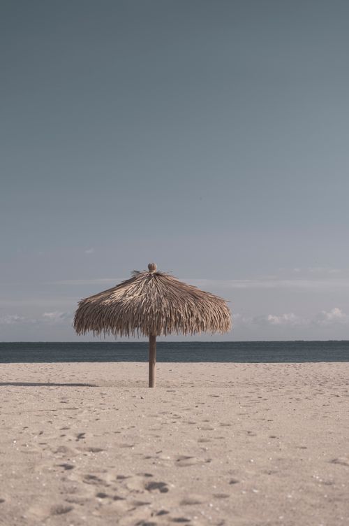 Free Serene beach setting featuring a straw umbrella under a clear sky, perfect for relaxation. Stock Photo