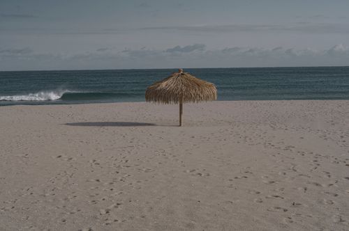 Free A peaceful sandy beach scene featuring a single tiki umbrella and gentle ocean waves. Stock Photo
