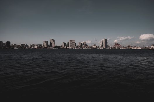 Dramatic city skyline viewed across a vast body of water, under a moody sky.