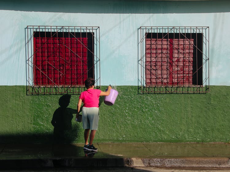 Woman Cleaning A Wall With A Bucket Of Water