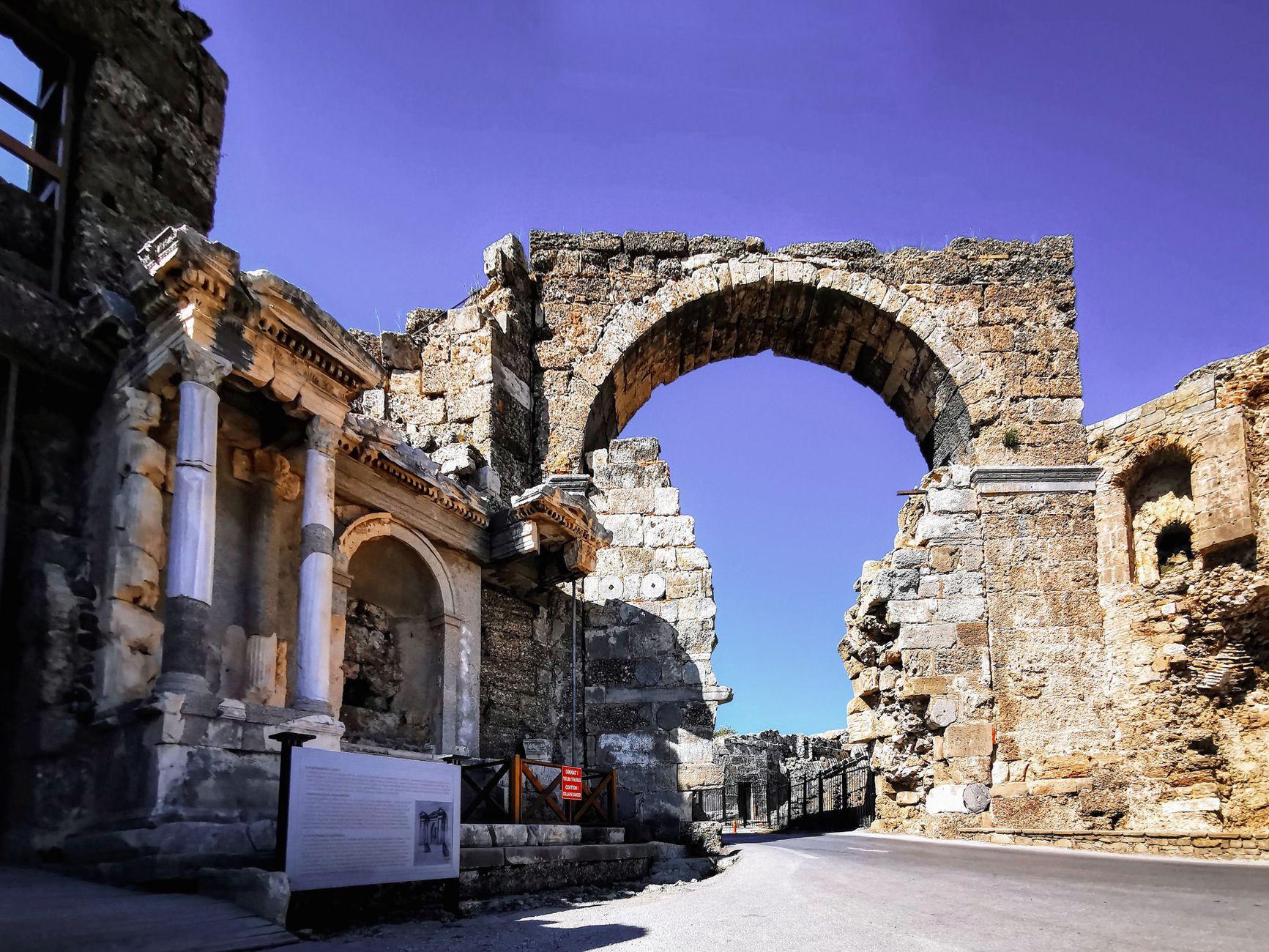 Explore the ancient Roman archway and ruins under a clear blue sky, showcasing historical architecture.