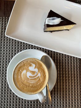 Top view of a latte with art and a slice of cheesecake on a table, offering a delicious break.