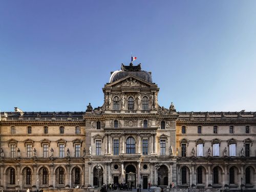 Free Front view of the historic Louvre Palace facade under a clear sky in Paris, France. Stock Photo