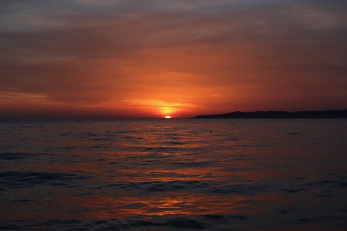 Free Capture of a dramatic sunset over the ocean with striking orange hues and gentle waves. Stock Photo