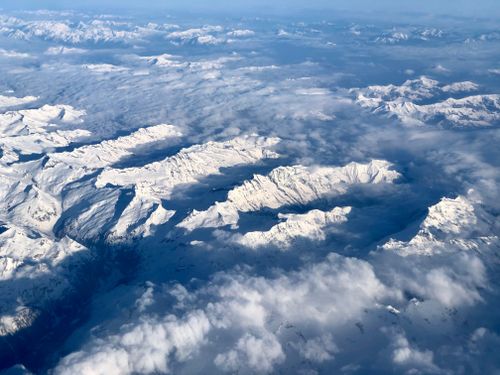 Free Stunning aerial view of a vast snowy mountain range covered in clouds, captured at high altitude. Stock Photo