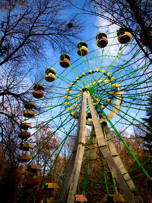 Free A vibrant Ferris wheel towering above bare trees against a blue sky in Rivne, Ukraine. Stock Photo