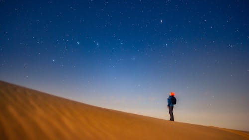 A person standing on top of a sand dune looking up at the stars