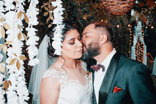 Bride and groom share a tender kiss beneath romantic floral decorations during their wedding.