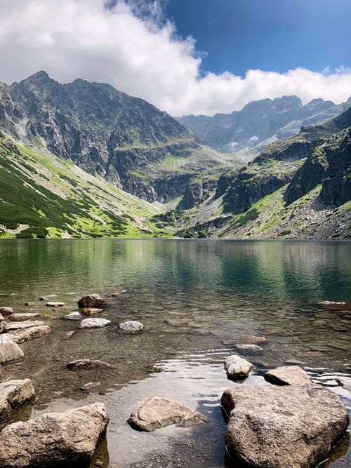Free A tranquil mountain lake surrounded by rocky peaks under a blue sky with clouds. Stock Photo