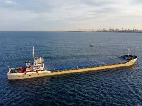 Free Aerial view of a cargo ship sailing near a bustling industrial harbor with cranes in the background. Stock Photo