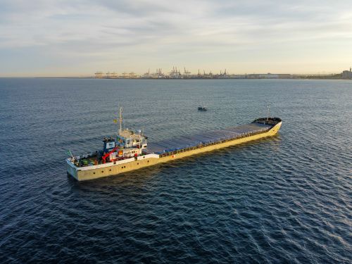 Free Aerial view of a cargo ship sailing near a busy industrial port at sunset. Stock Photo