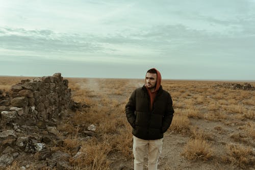 Man in Jacket Standing near Damaged Wall on Grassland