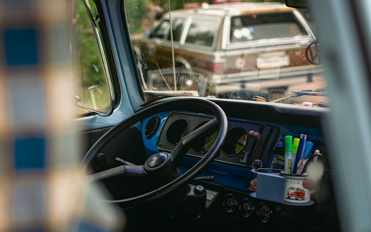 Interior view of a vintage car featuring a classic dashboard, steering wheel, and outdoor view.