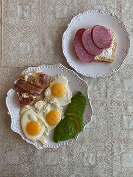 Top view of a delicious breakfast featuring eggs, ham, salami, and sliced avocado.
