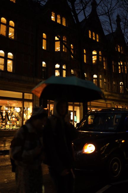 Rainy night urban scene with silhouettes and illuminated building.