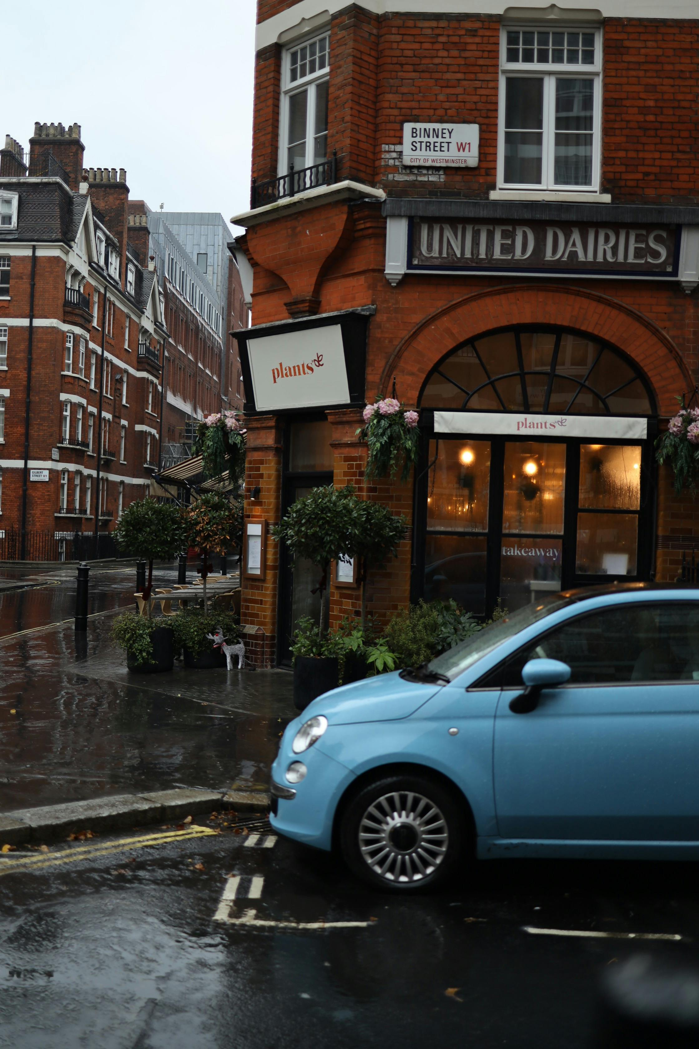 Free Urban corner scene with red brick building and blue car in rain. Stock Photo