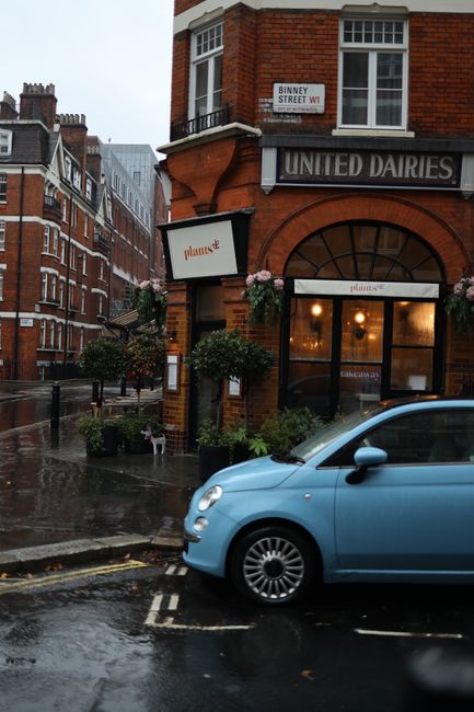 Urban corner scene with red brick building and blue car in rain.