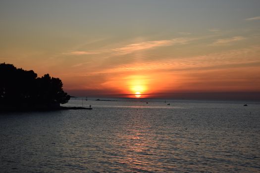 Capture the serene sunset over the Adriatic Sea, Poreč, Croatia, with vibrant orange hues.